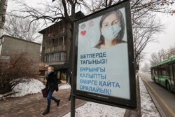 Қала әкімдігінің маска тағуға шақырған постерінің жанынан өтіп бара жатқан қыз. Алматы 13 желтоқсан 2020 жыл.